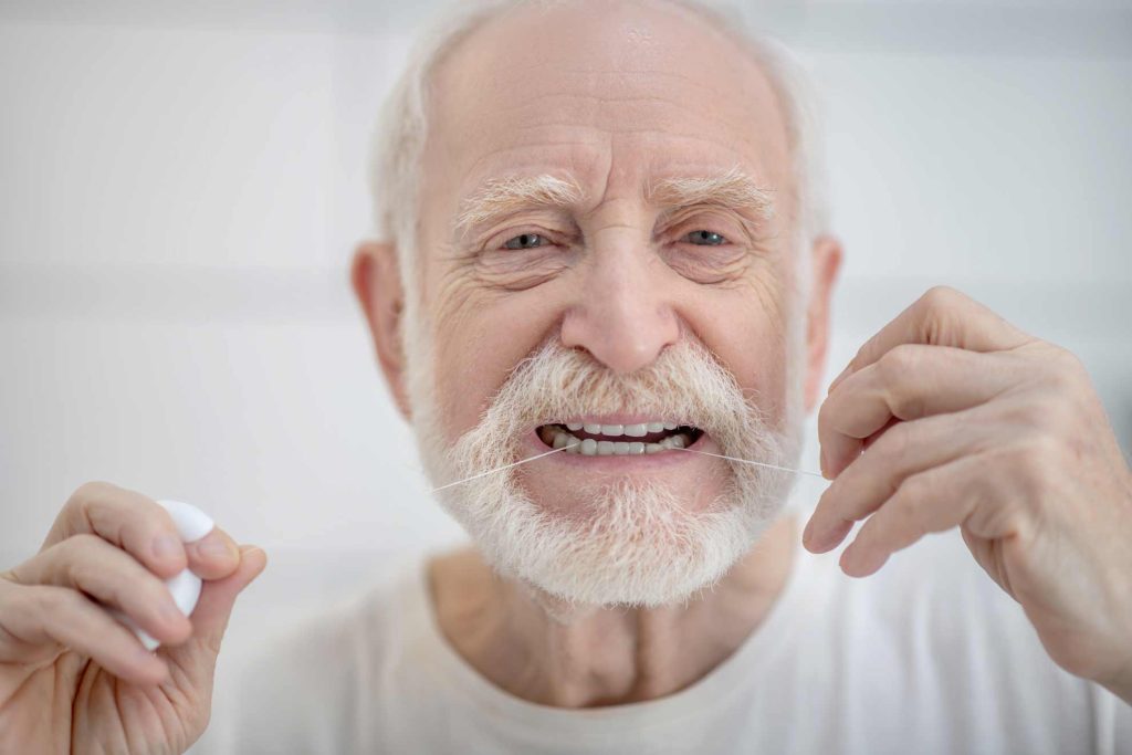 hombre mayor utilizando el hilo dental en la limpieza bucal